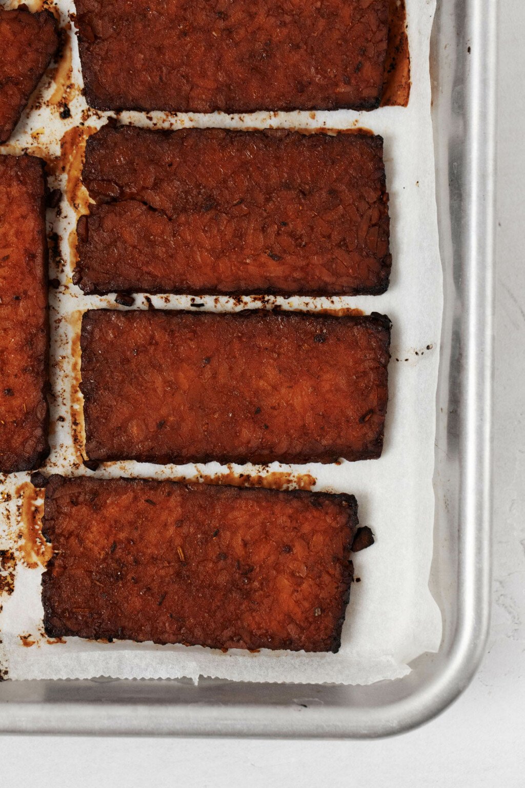 Baked strips of a plant-based protein rest on a lined baking sheet.