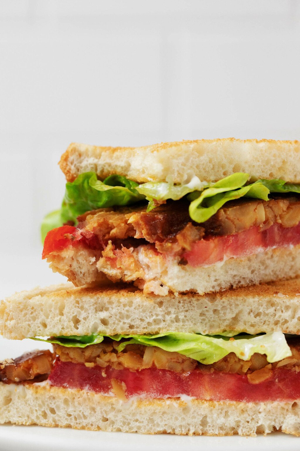 A close up image of a vegan BLT sandwich, prepared with tempeh bacon.