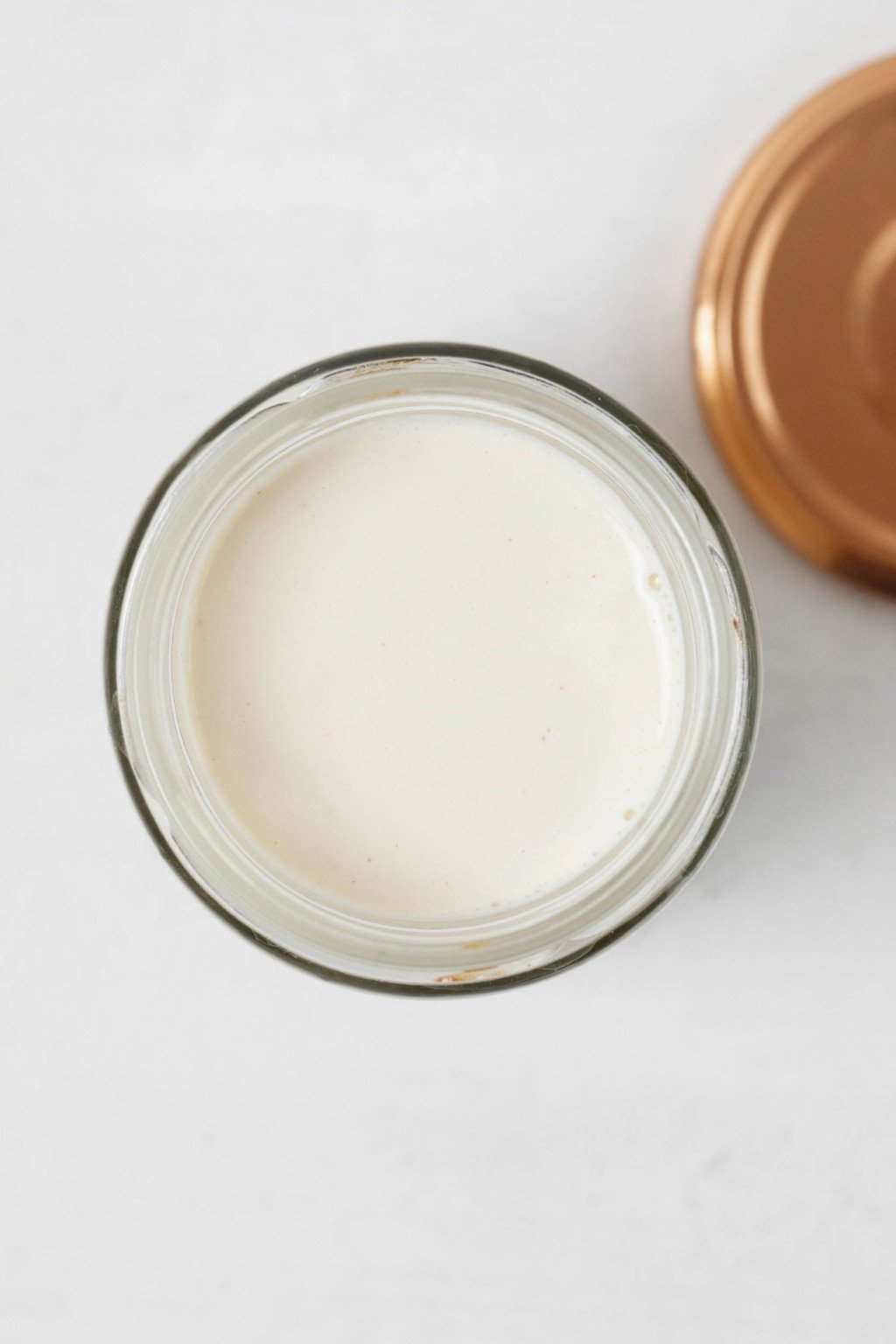 A mason jar with a metal lid is resting on a white surface. The jar contains a white sauce.