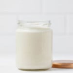 A mason jar has been filled with a vegan mayo, made from cashews. It rests on a white surface.
