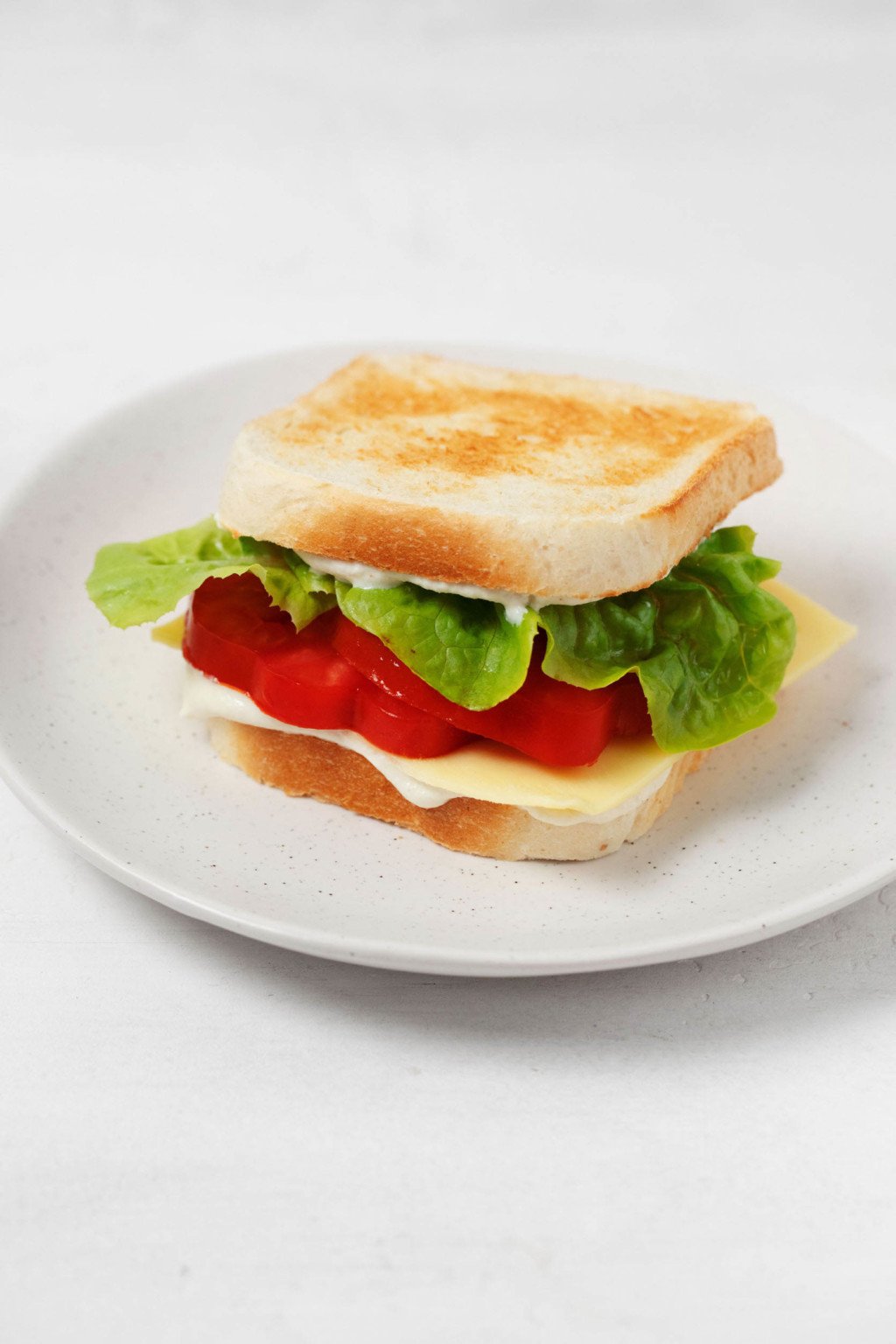 A tomato, lettuce, and cheese sandwich is sitting on a small, round white plate.