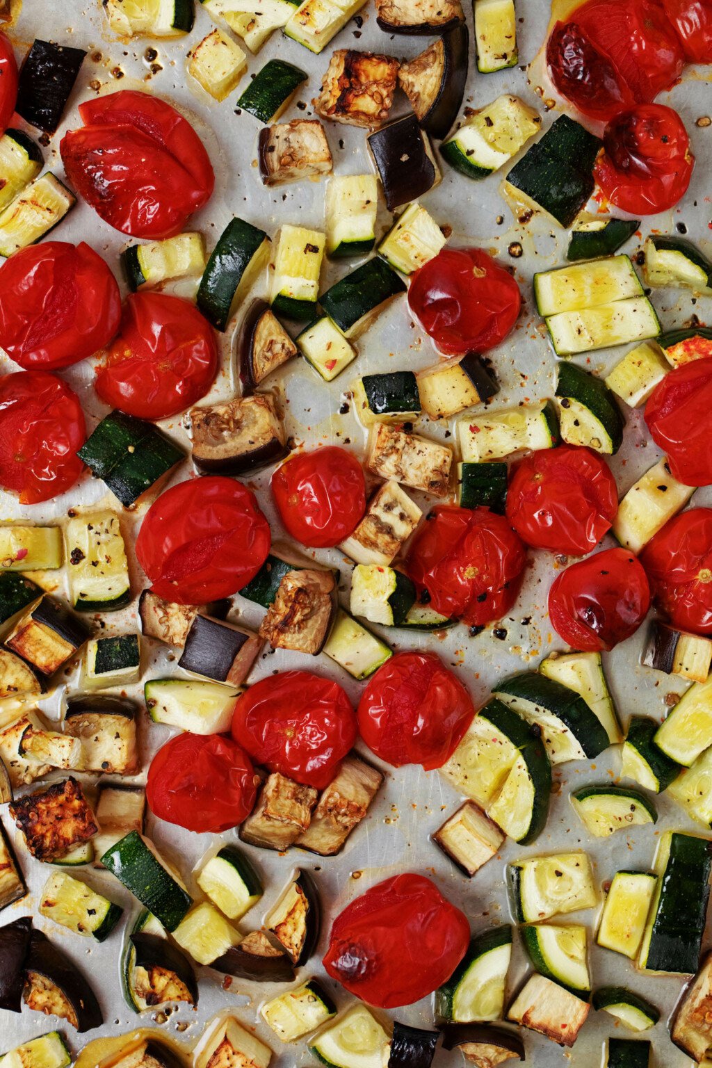 A close up image of roasted grape tomatoes, zucchini and eggplant on a baking tray.