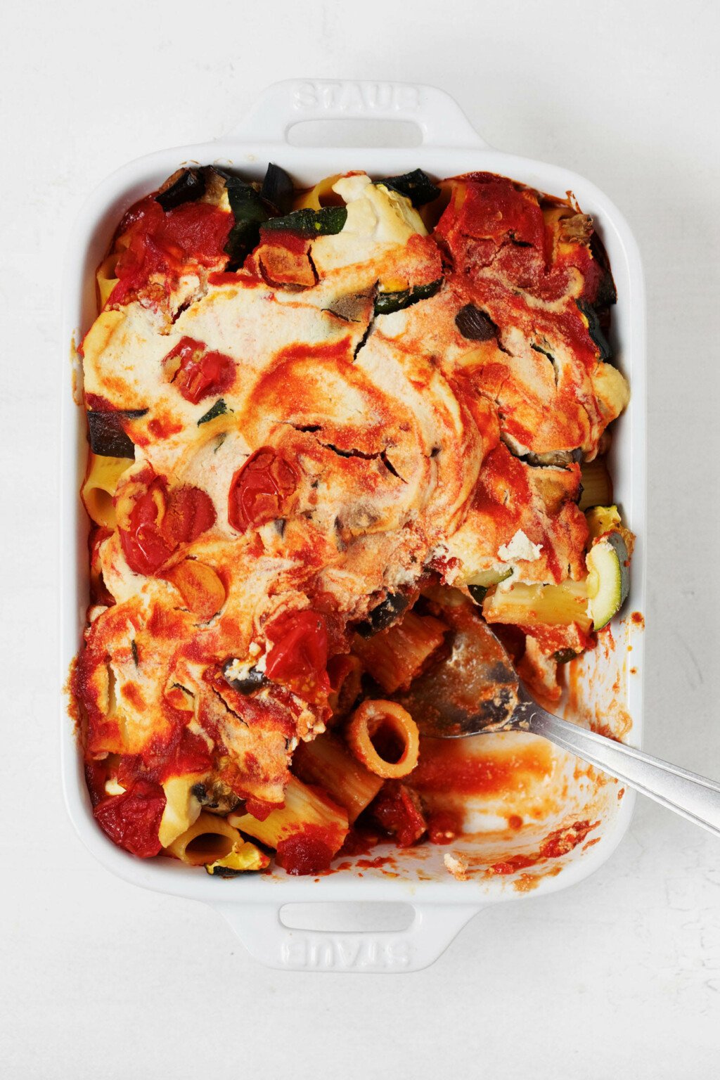 A white, rectangular baking dish holds a vegan pasta bake with ricotta and roasted summer vegetables.