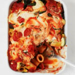 A white, rectangular baking dish holds a vegan pasta bake with ricotta and roasted summer vegetables.