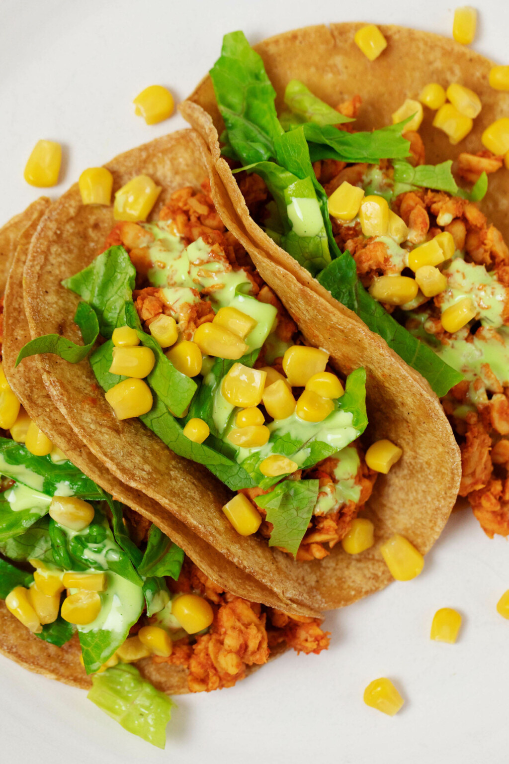 An overhead image of vegan tempeh tacos with corn, lettuce, and a creamy dressing.
