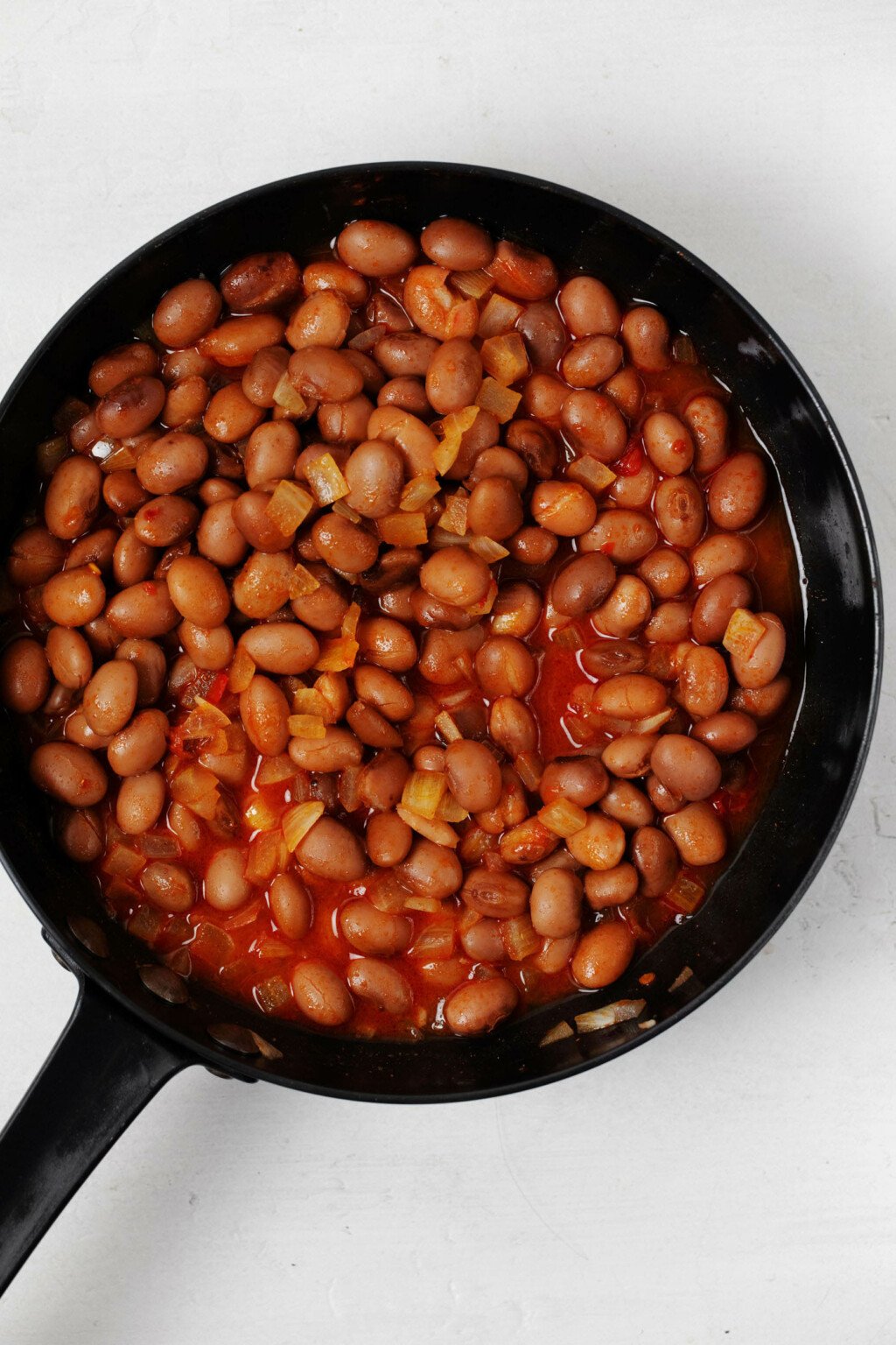 A cast iron skillet is filled with pinto beans, tomato, and spices.