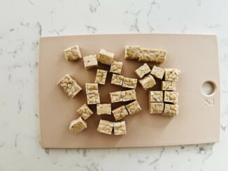 A small, pink cutting board has been used to cut a block of tempeh into cubes.