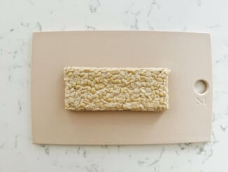 A rectangular block of tempeh rests on a small, pink cutting board.