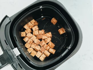 The black basket of an air fryer holds seasoned tempeh nuggets, prior to air frying.