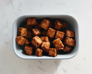 A small, rectangular blue storage container holds recently cooked, lightly browned air fryer tempeh nuggets.