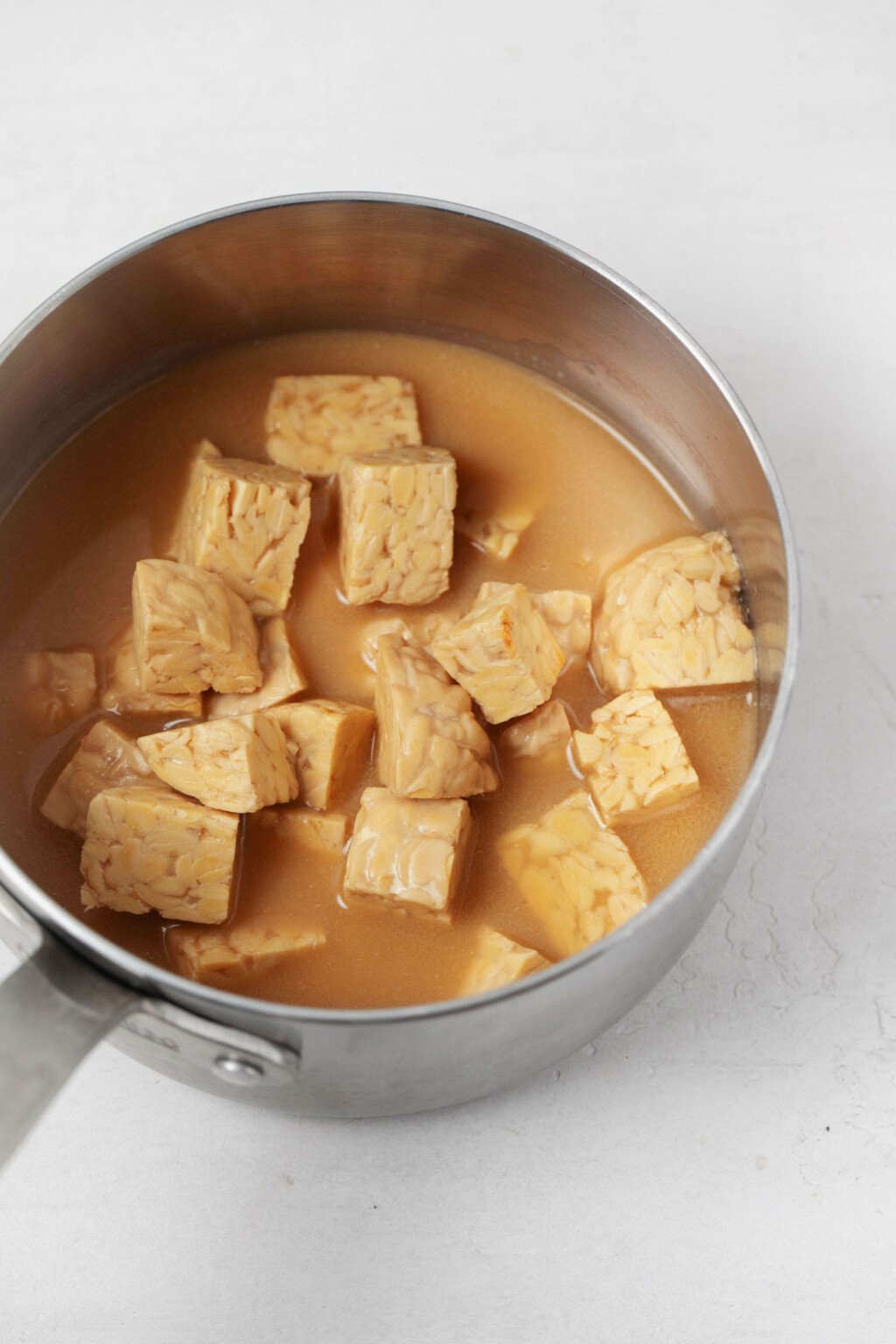 Tempeh and broth are simmered in a small saucepan.