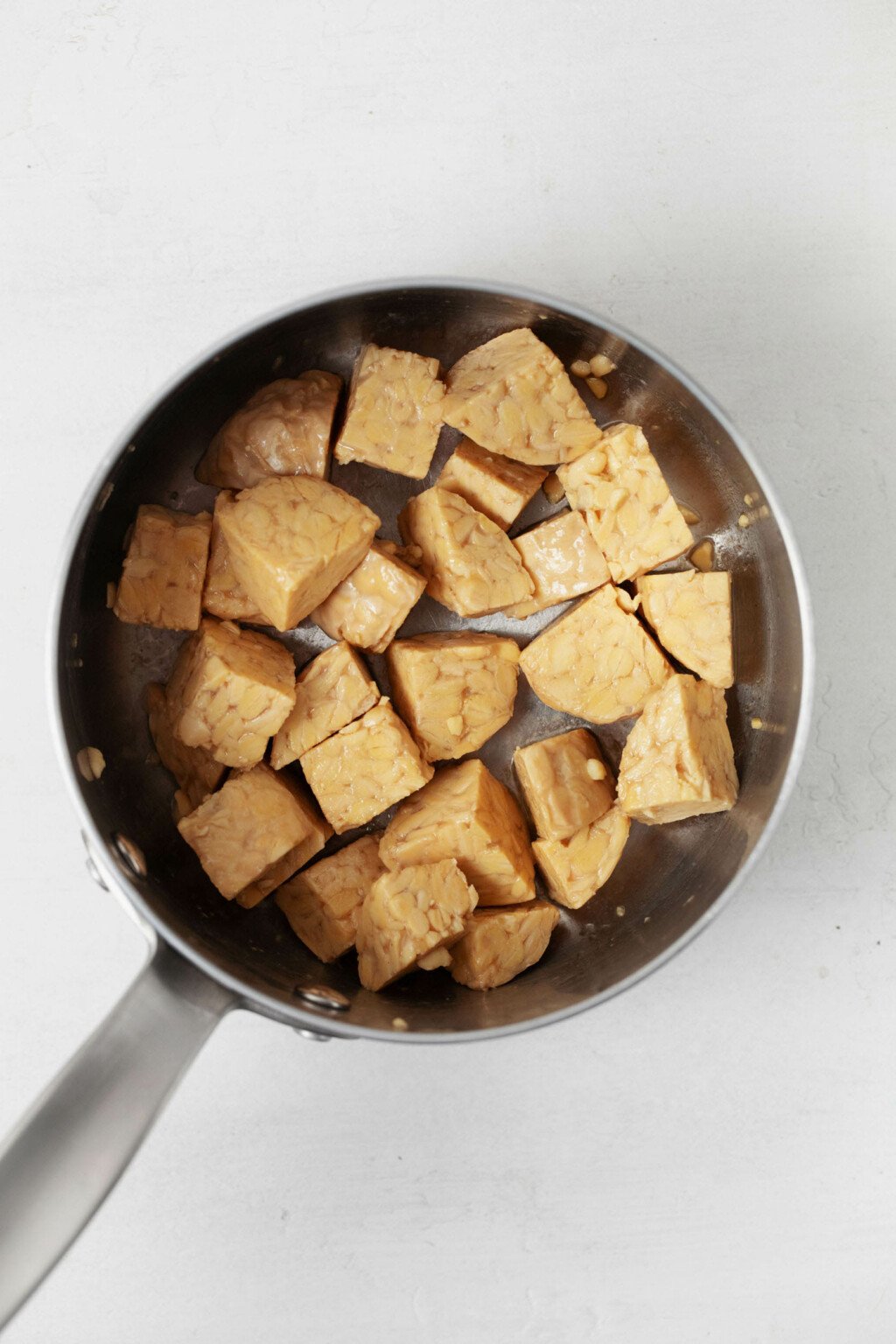 A sauce pot holds cubes of tempeh, which have been seasoned with broth and spices.