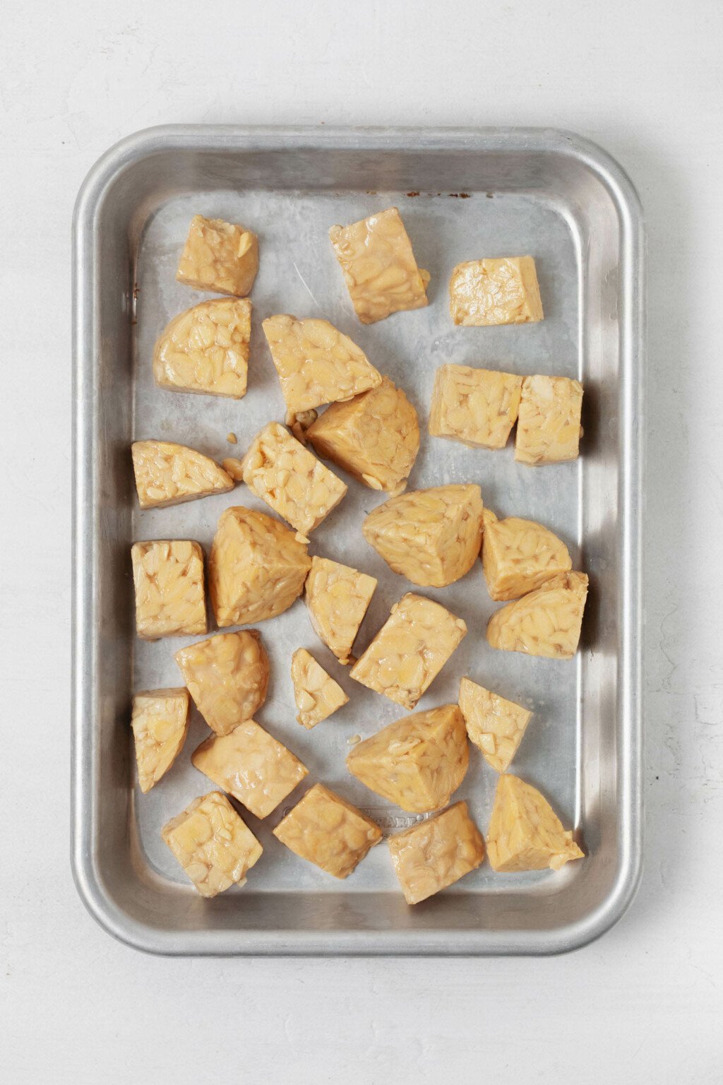 A small baking tray holds cubes of tempeh, which will become seasoned tempeh nuggets.