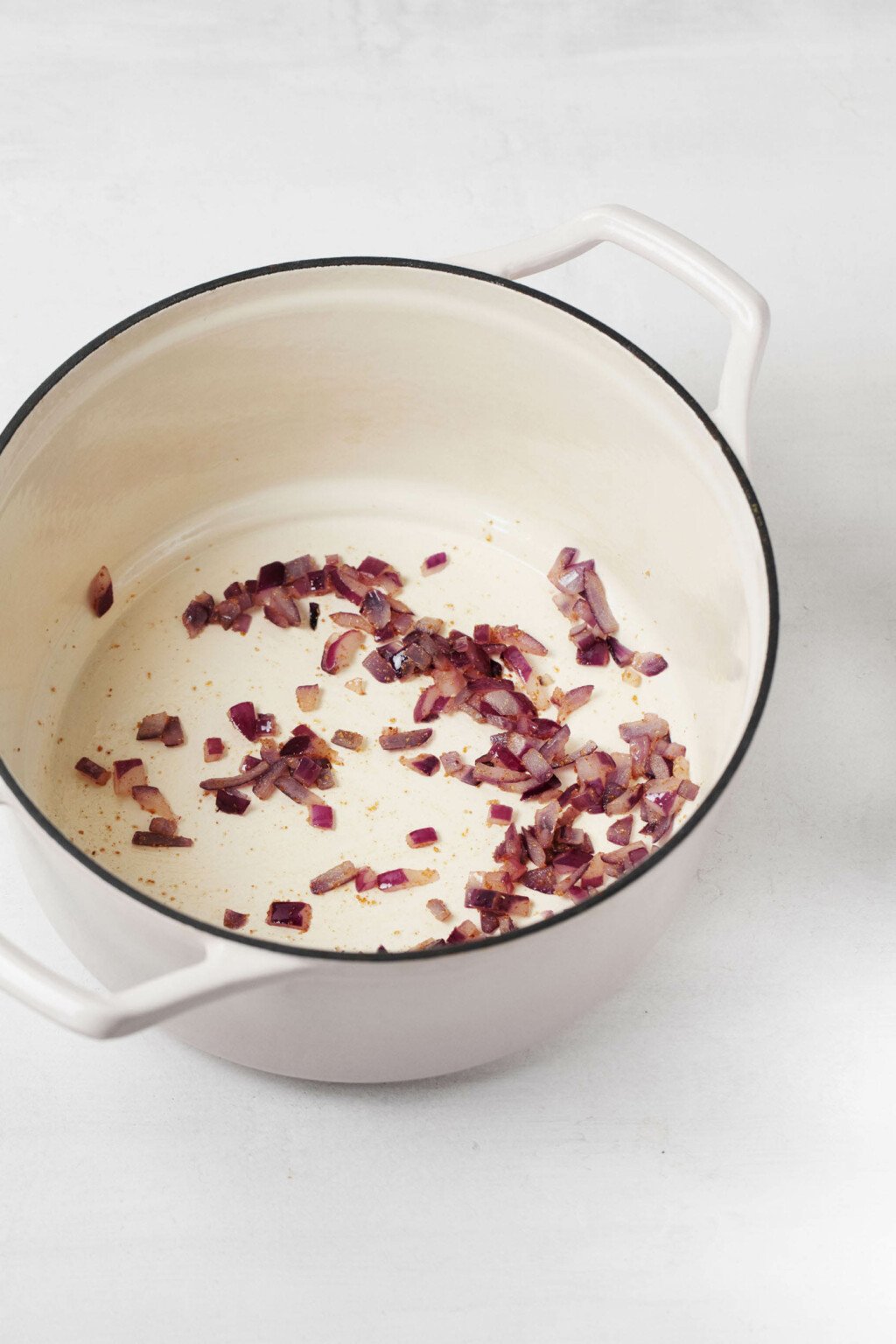 Red onions are being fried in a white pot with a black rim.
