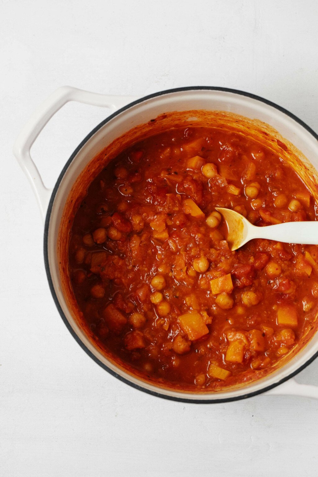 A large, white pot holds a mixture of tomatoes, butternut squash, and chickpeas.