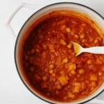 A large, white pot holds a mixture of tomatoes, butternut squash, and chickpeas.