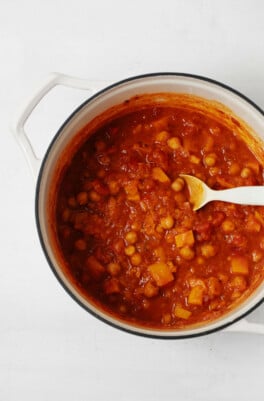 A large, white pot holds a mixture of tomatoes, butternut squash, and chickpeas.