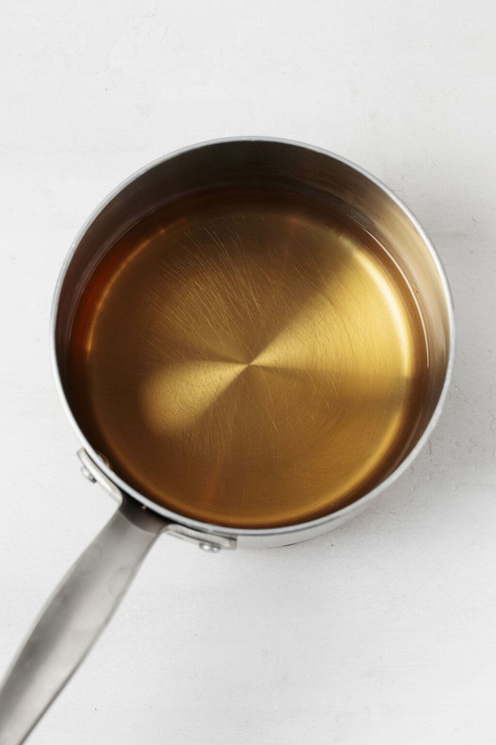 A small, silver saucepan contains a mixture of vinegar and water. It's resting on a white surface.