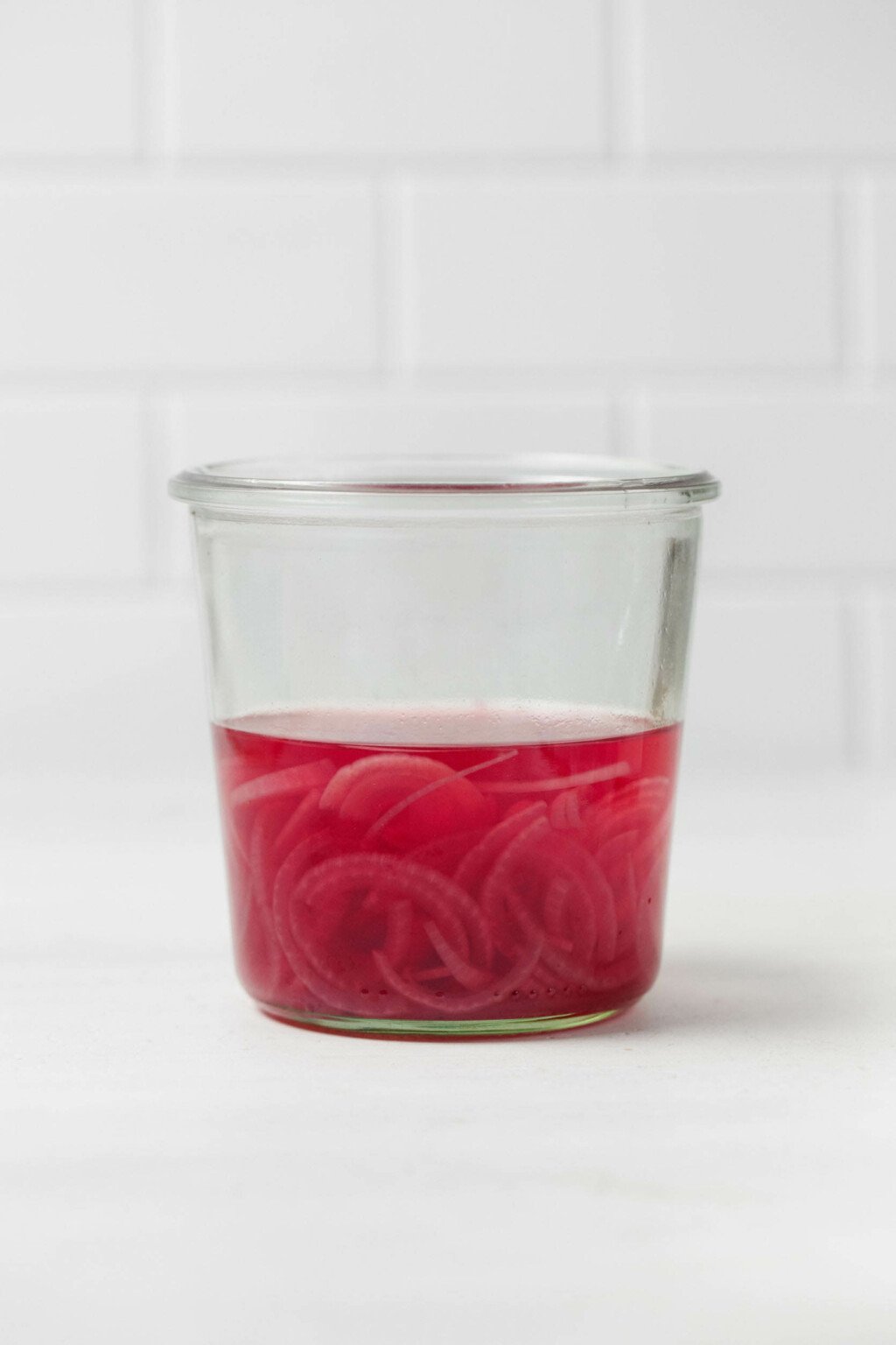 A mason jar contains bright pink, quick pickled red onions in brine.
