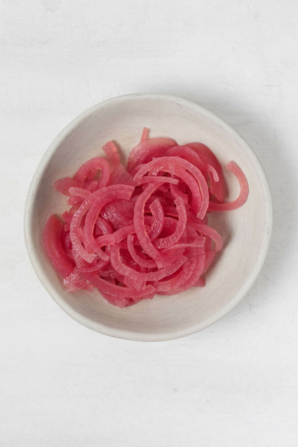 A small, white pinch bowl contains bright pink, quick pickled onions.