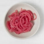 A small, white pinch bowl contains bright pink, quick pickled onions.