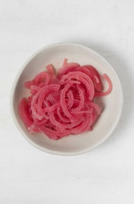 A small, white pinch bowl contains bright pink, quick pickled onions.