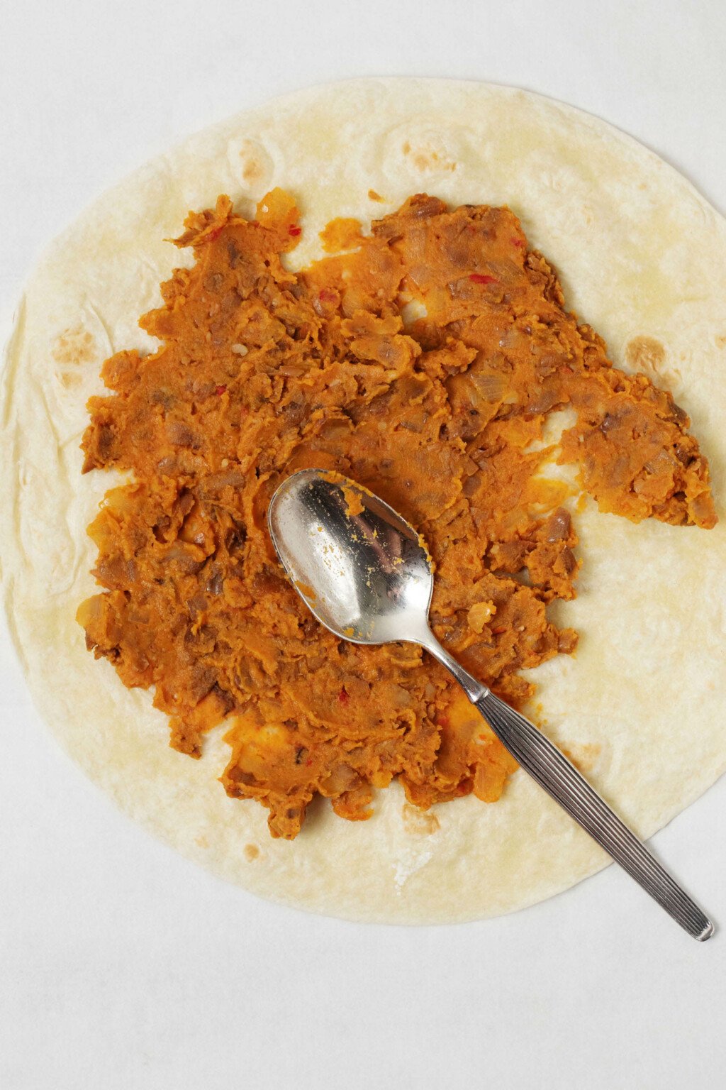 A tortilla is being covered in a refried bean spread.