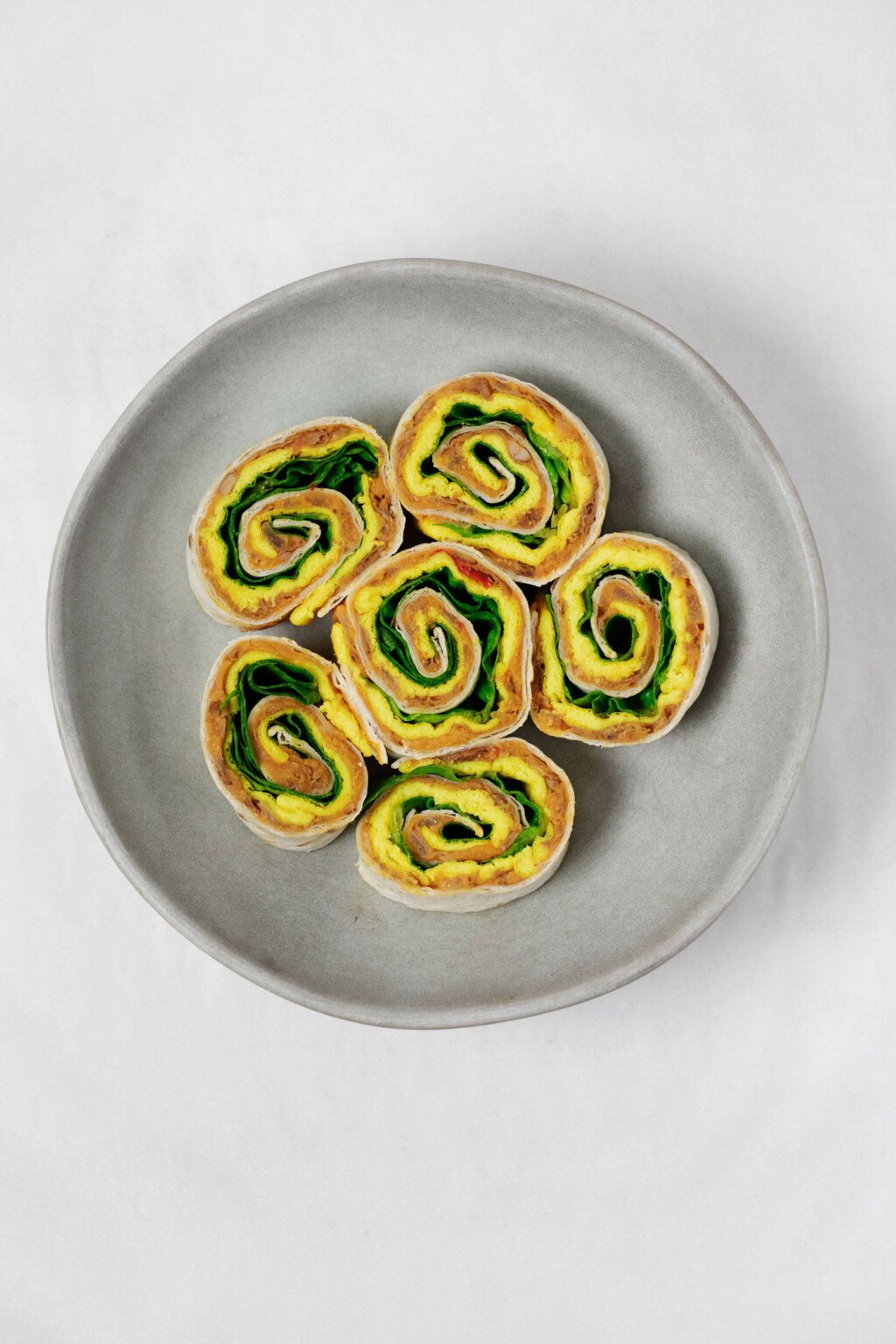 Vegan breakfast pinwheels, made with refried beans and layers of a yellow vegan egg mixture, have been cut and placed on a small, round plate.