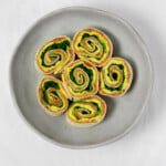 Vegan breakfast pinwheels, made with refried beans and layers of a yellow vegan egg mixture, have been cut and placed on a small, round plate.