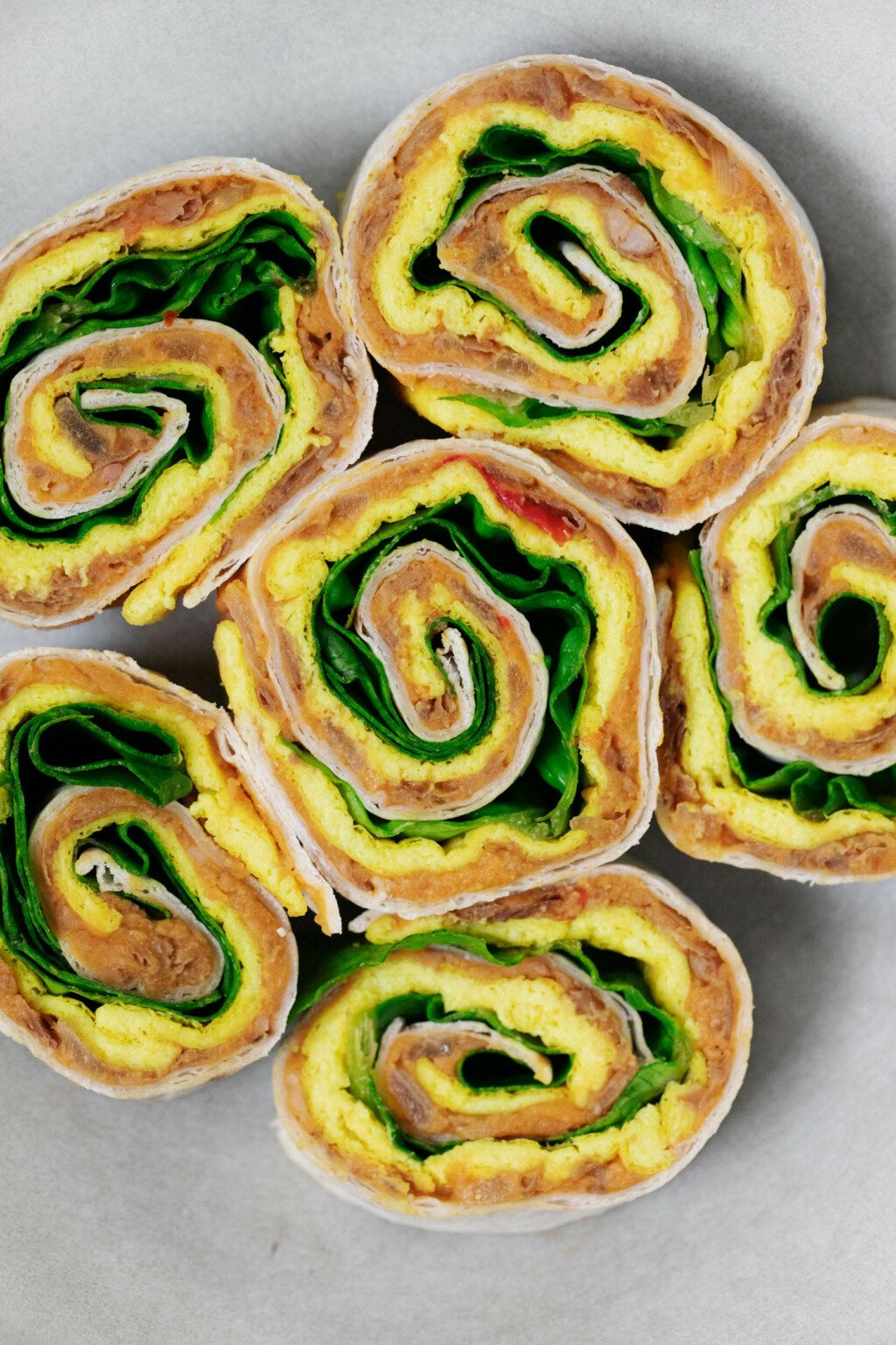 A cross-section of colorful vegan breakfast pinwheels, made with refried beans, tofu, and greens.