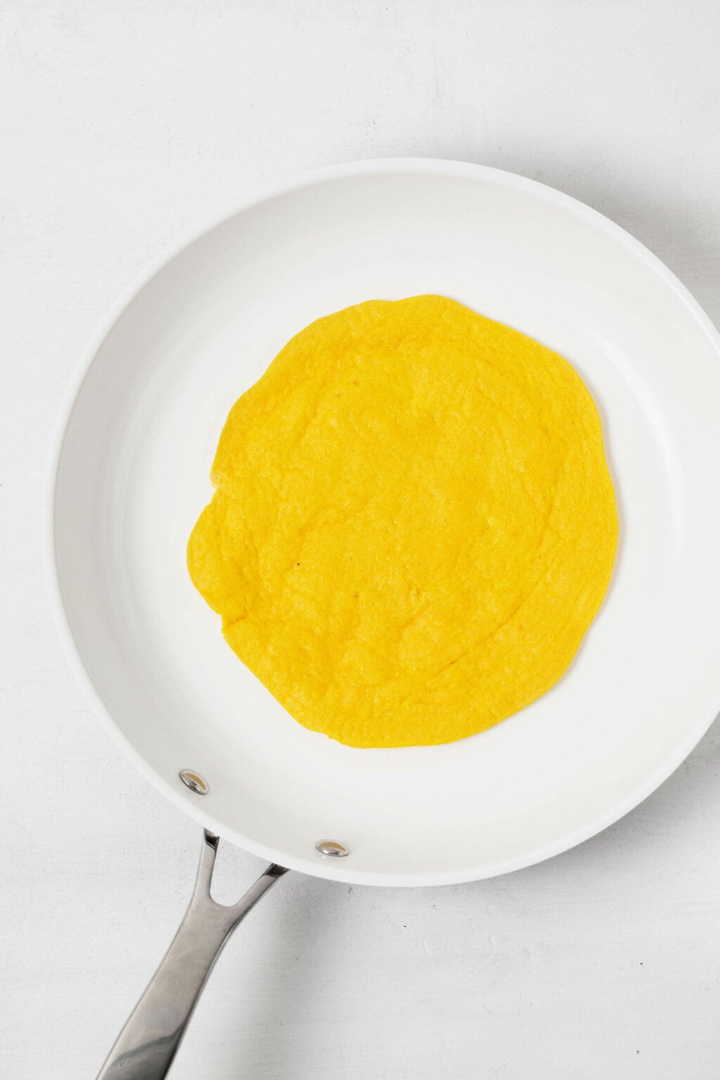 Ένα μικρό, λευκό αντικολλητικό τηγάνι χρησιμοποιείται για να αναποδογυρίσετε ένα μείγμα αυγών με βάση τα φυτά.