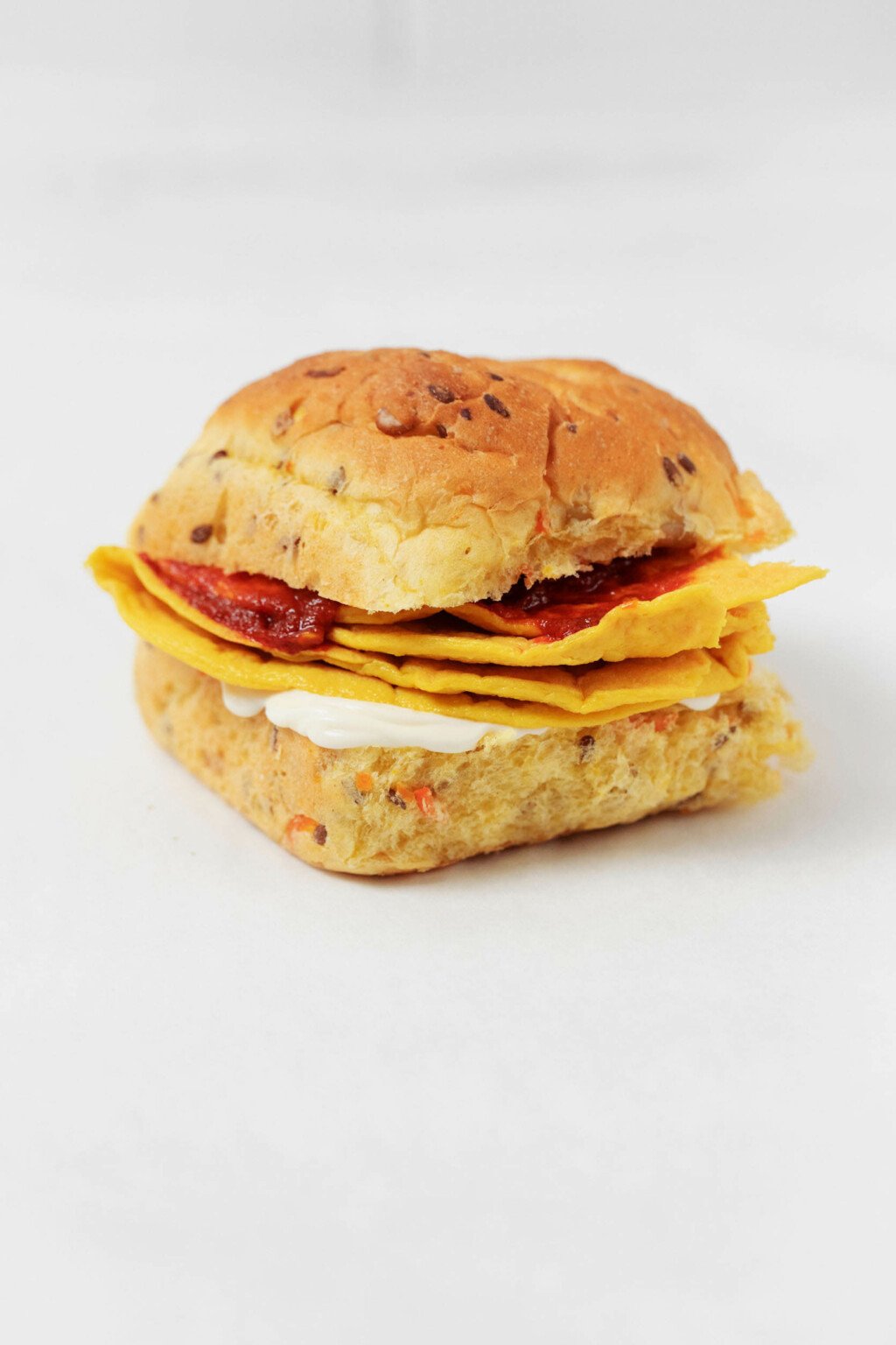 A breakfast sandwich on an herbed bun is resting on a white surface.