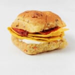 A breakfast sandwich on an herbed bun is resting on a white surface.