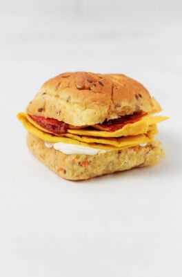 A breakfast sandwich on an herbed bun is resting on a white surface.