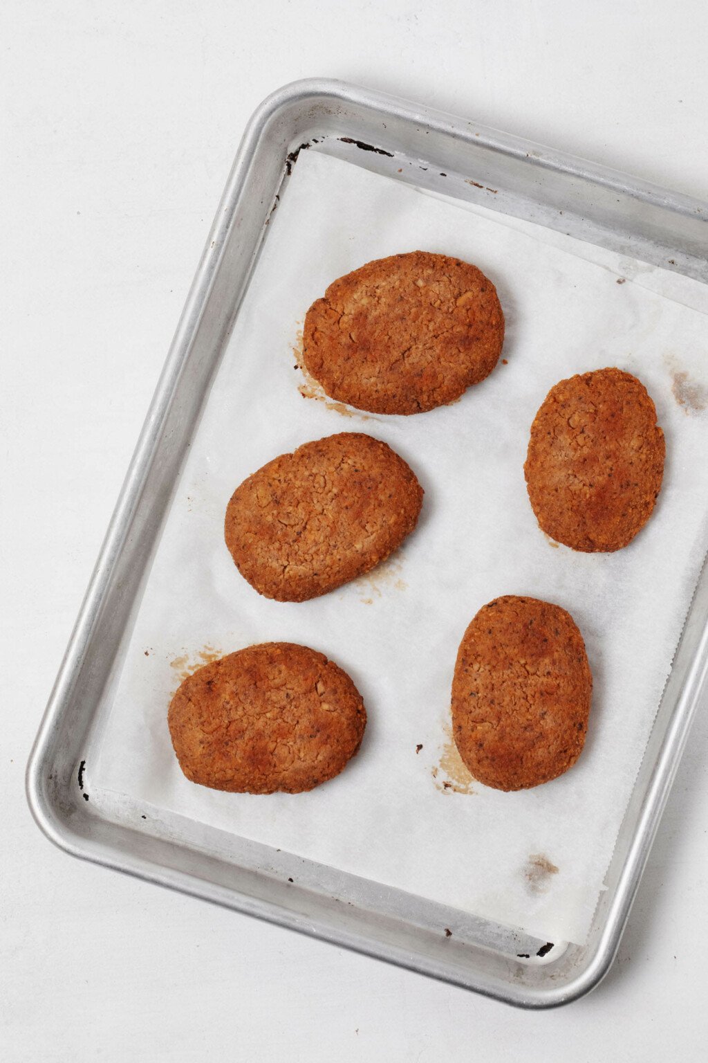 Patties of tempeh, which have been formed to look like mini "steaks," are laid on parchment on a baking sheet.