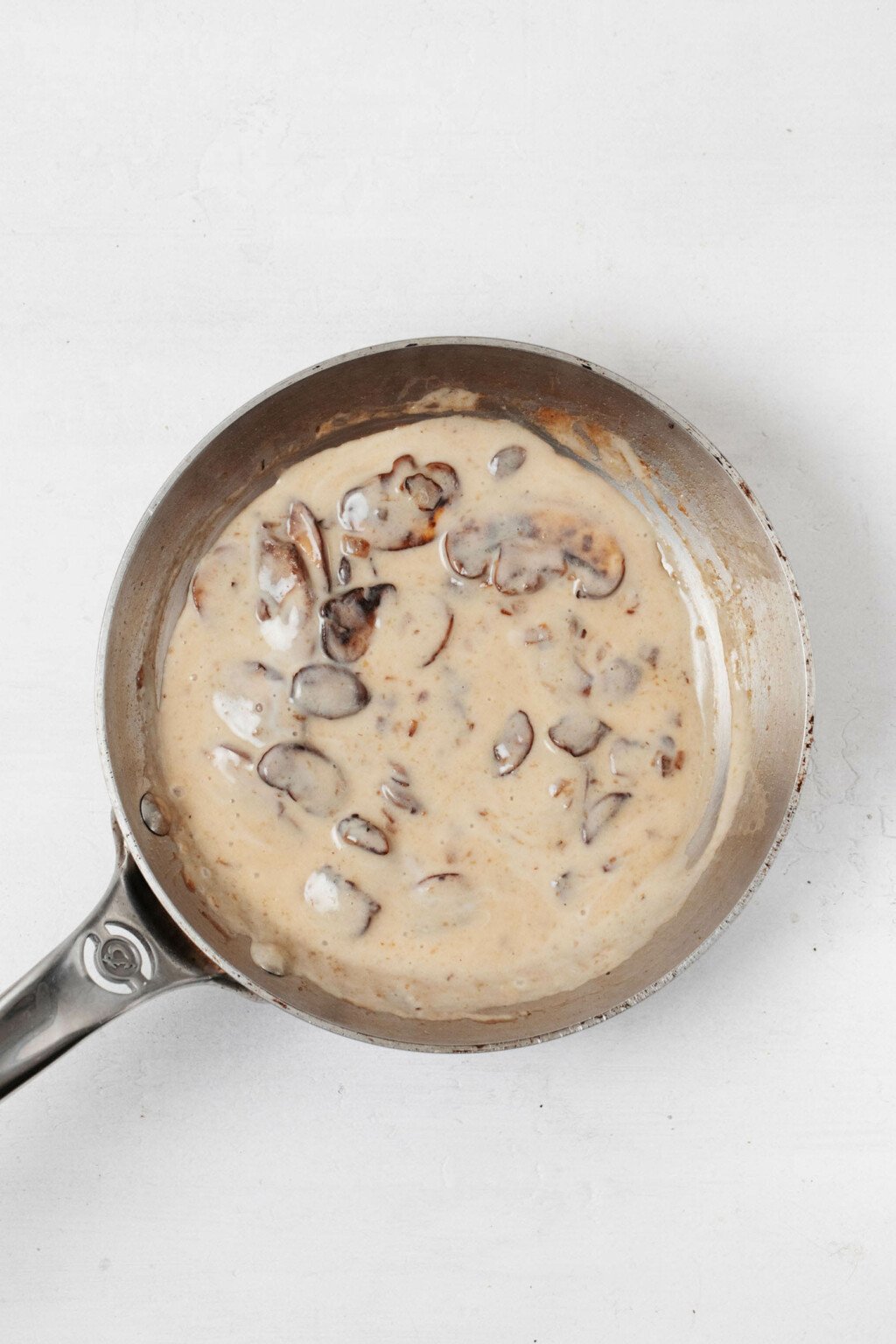 A small, stainless steel frying pan is being used to make a mushroom gravy.