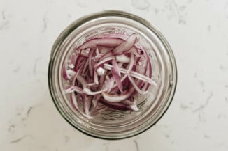 A wide-mouthed mason jar contains thinly sliced, red onions.