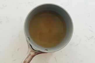 A small, gray saucepan contains a mixture of vinegar and water. It's resting on a white surface.