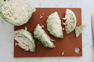 Eight wedges of cabbage are being cut on a red cutting board.