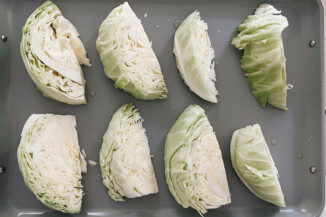 A gray baking sheet holds cabbage wedges, which have been drizzled with oil.