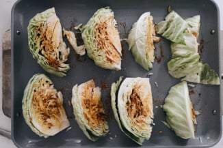 Cabbage wedges have been covered in a spice mixture prior to roasting on a gray baking sheet.