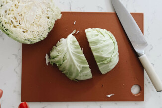 A cabbage is being cut in a red colored board.