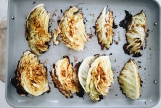 Roasted wedges of cabbage steak are laid on a gray baking sheet.
