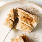 Two slices of vegan tiramisu are arranged on a small ceramic plate. A fork cuts into one of the slices.