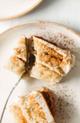 Two slices of vegan tiramisu are arranged on a small ceramic plate. A fork cuts into one of the slices.