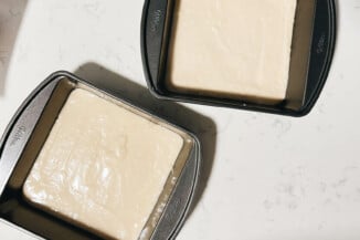 Two square baking pans have been filled with a pale yellow cake batter.