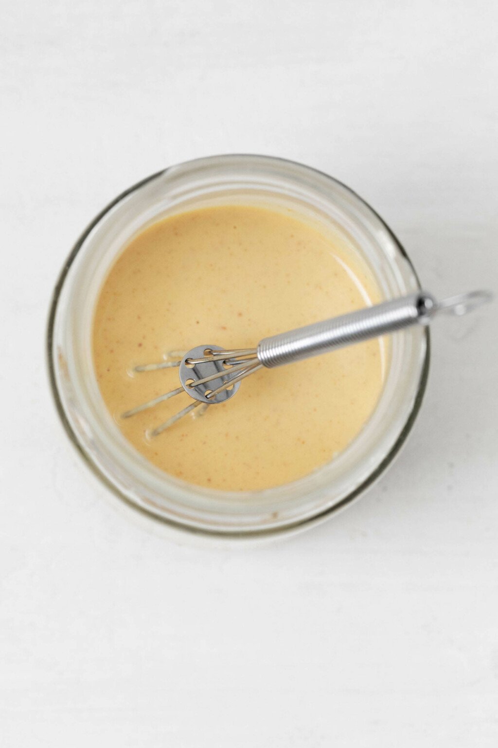 A Dijon lemon tahini dressing is being whisked in a small, round, Pyrex bowl.
