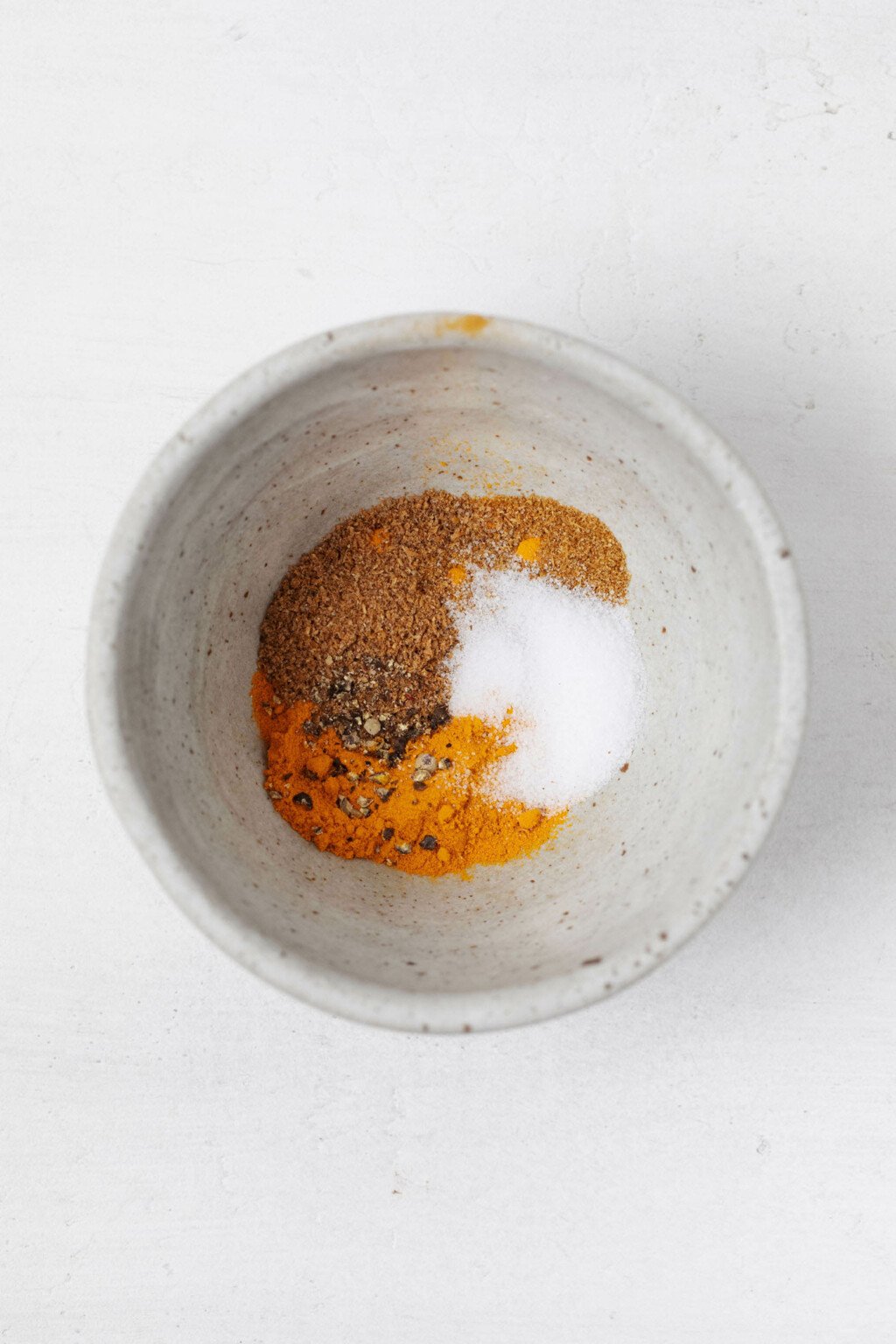 Ένα μικρό, κεραμικό μπολ περιέχει ένα μείγμα μπαχαρικών σε χρυσή απόχρωση.