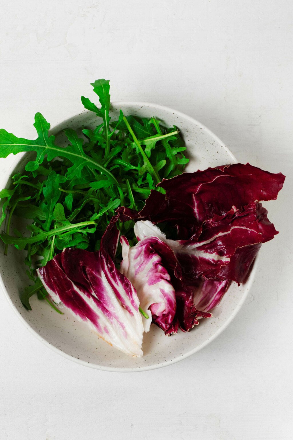 A round white plate is covered with radicchio and arugula.