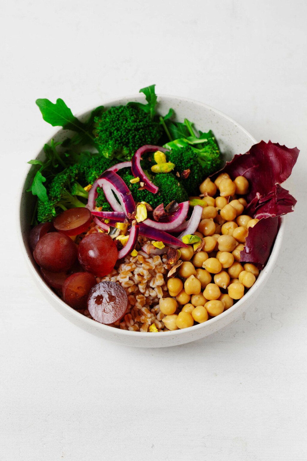 A colorful bowl with chickpeas, vegetables and pickled onions resting on a white surface.